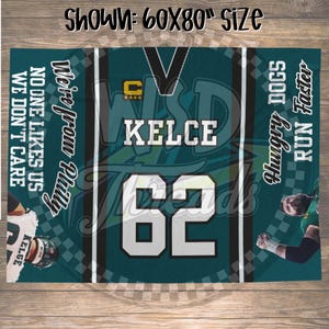 Puede incluir: Una manta turquesa y blanca con el texto "KELCE" y el número "62" en blanco. La manta también presenta las frases "We're from Philly", "No one likes us, we don't care", "Hungry Dogs" y "Run Faster".