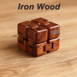 Puede incluir: Un cubo infinito de madera con la palabra "TIME" en un lado. El cubo es de madera marr&oacute;n oscuro y est&aacute; sobre una superficie de madera. El texto "Iron Wood" est&aacute; encima del cubo.