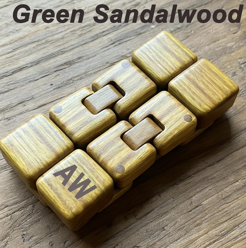 Puede incluir: Un juguete fidget de madera de s&aacute;ndalo verde. El juguete est&aacute; compuesto por bloques cuadrados conectados. Uno de los bloques tiene las iniciales "AW". El texto "Green Sandalwood" est&aacute; en la parte superior de la imagen.