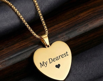 May include: A gold-colored necklace with a heart-shaped pendant. The pendant has the words "My Dearest" and a small heart symbol engraved on it. The necklace chain is a box chain style.