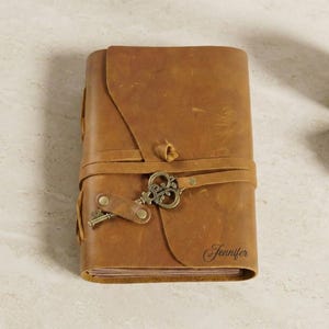 May include: A brown leather journal with a flap closure and a decorative key clasp. The journal is secured with a leather strap and features the name "Jennifer" on the cover. The journal is rectangular in shape.