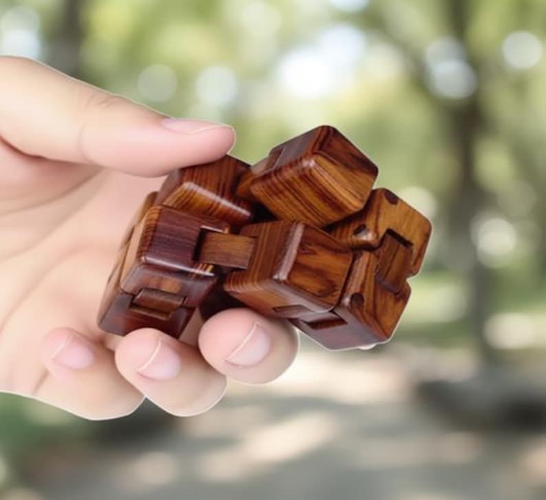 Puede incluir: Un cubo de rompecabezas de madera con un dise&ntilde;o entrelazado complejo. El cubo est&aacute; hecho de madera marr&oacute;n oscura con patrones de vetas visibles. El rompecabezas se sostiene en una mano contra un fondo verde borroso.