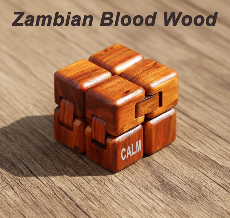Puede incluir: Un cubo fidget de madera de Zambian Blood Wood. El cubo es de color marr&oacute;n c&aacute;lido con vetas de madera visibles. La palabra "CALM" est&aacute; impresa en una de las caras del cubo. El texto "Zambian Blood Wood" est&aacute; en la parte superior de la imagen.