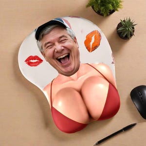 Könnte beinhalten: Ergonomische Mausunterlage mit einem humorvollen Design. Die Unterlage hat einen weißen Hintergrund mit einem lächelnden Gesicht, das einen Hut und ein rotes Bikini-Oberteil trägt. Rote Lippenstiftkussspuren sind ebenfalls auf der Unterlage aufgedruckt. Eine schwarze Maus und ein Stift sind ebenfalls sichtbar.