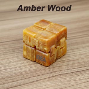 Puede incluir: Un cubo de madera de color &aacute;mbar con la palabra "IDEA" impresa en un lado. La parte superior del cubo tiene las palabras "Amber Wood" impresas en negro. El cubo est&aacute; hecho de varios bloques conectados.