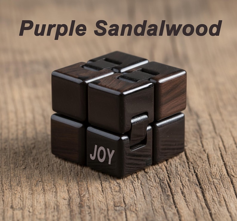 Puede incluir: Un juguete cubo fidget de madera de s&aacute;ndalo p&uacute;rpura. El cubo es de color marr&oacute;n oscuro con vetas de madera visibles y la palabra "JOY" est&aacute; impresa en uno de los bloques. El texto "Purple Sandalwood" est&aacute; encima del cubo.