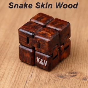 Puede incluir: Un cubo de madera hecho de madera de piel de serpiente. El cubo es de color marr&oacute;n oscuro con vetas de madera visibles. Las letras "K&N" est&aacute;n grabadas en una de las caras del cubo. El texto "Snake Skin Wood" est&aacute; en la parte superior de la imagen.