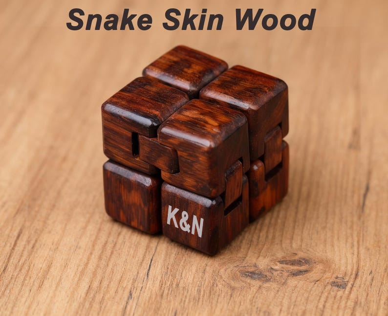 Puede incluir: Un cubo de madera hecho de madera de piel de serpiente. El cubo es de color marr&oacute;n oscuro con vetas de madera visibles. Las letras "K&N" est&aacute;n grabadas en una de las caras del cubo. El texto "Snake Skin Wood" est&aacute; en la parte superior de la imagen.