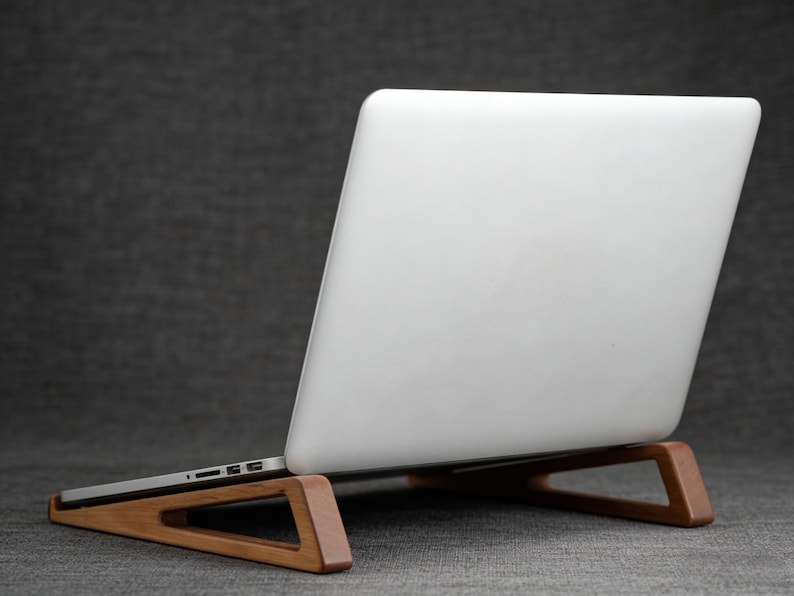 May include: A wooden laptop stand with a white laptop resting on it. The stand is made of light brown wood and has a triangular design. The laptop is white and has a silver edge.