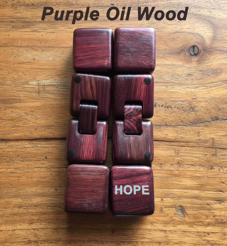 Puede incluir: Una pulsera de madera hecha de bloques cuadrados e interconectados de madera de aceite p&uacute;rpura. La palabra "HOPE" est&aacute; impresa en blanco en uno de los bloques. El texto "Purple Oil Wood" est&aacute; en la parte superior de la imagen.