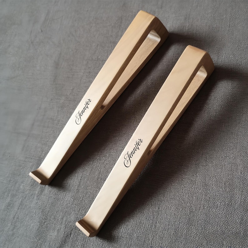 May include: Two light-colored wooden laptop stands with a minimalist design. Each stand has a sloped surface and a cutout for ventilation. The name "Jennifer" is elegantly inscribed on each stand.