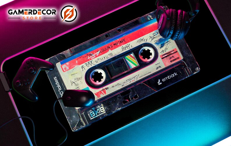 May include: A gaming mousepad featuring a retro cassette tape design with the text "ALGUNS MIXTAPE". A black controller, mouse, and headphones are also visible. The mousepad has a black background with pink and blue neon accents.