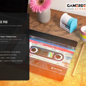 May include: A slim mouse pad with a retro cassette tape design. The pad is made of high-density foam with a rubber base, measuring 8" x 8". Other desk accessories include a pencil, tape dispenser, and a small vase with a pink flower.
