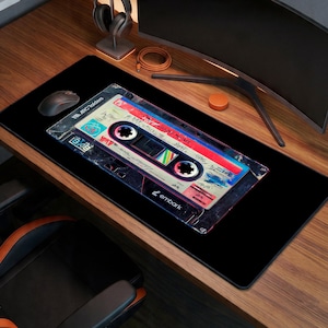 May include: Black rectangular mouse pad featuring a retro cassette tape design. The tape has a colorful label with text and a vintage aesthetic. The mouse pad has the word "embark" printed on it.