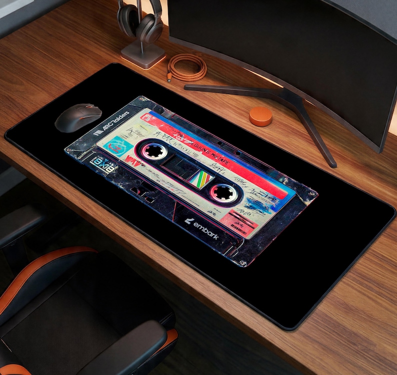 May include: Black rectangular mouse pad featuring a retro cassette tape design. The tape has a colorful label with text and a vintage aesthetic. The mouse pad has the word "embark" printed on it.