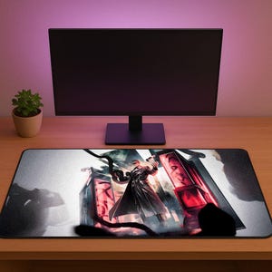 Puede incluir: Alfombrilla de ratón rectangular con una ilustración detallada de una figura con un abrigo largo, sosteniendo un arma, con detalles en rojo y un fondo oscuro. La alfombrilla está colocada sobre un escritorio de madera, con un monitor de ordenador y una pequeña planta en maceta en el fondo.
