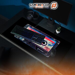 May include: A black gaming keyboard with illuminated keys rests on a mousepad with a retro cassette tape design. The mousepad features red, blue, and white accents, and the word "embark" is visible. The GamerDecor Store logo is in the top right.