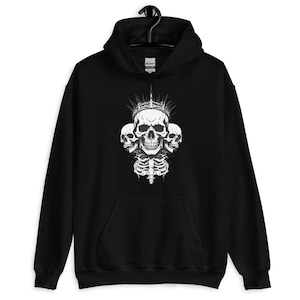 May include: Black hooded sweatshirt featuring a white graphic of three skulls, a crown, and a rib cage. The design is centered on the front of the sweatshirt. The sweatshirt has a front pocket and a drawstring hood.