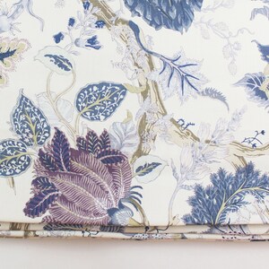 May include: A white fabric with a blue, purple, and gold floral pattern. The fabric has a subtle sheen and a soft texture.