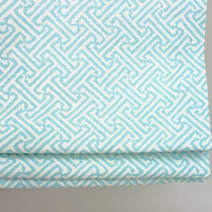 May include: A light blue roman shade with a white geometric pattern. The shade is made of a woven fabric and has a subtle texture.