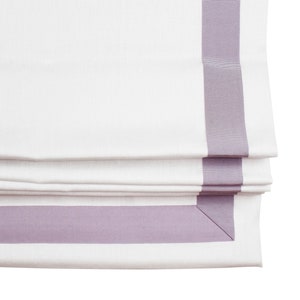 May include: White roman shade with a lavender trim. The shade is folded and the trim is visible on the top and bottom of the shade.