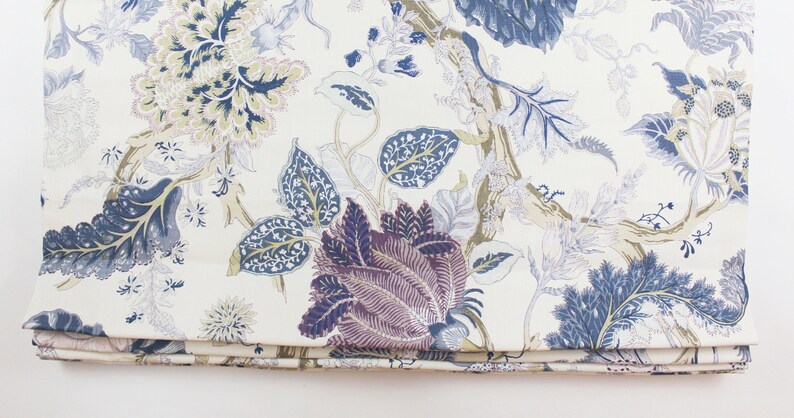 May include: A white fabric with a blue, purple, and gold floral pattern. The fabric has a subtle sheen and a soft texture.