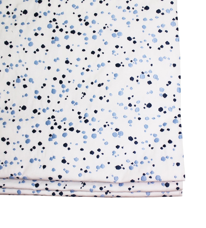 May include: White fabric with a blue and black speckled pattern. The fabric is folded in thirds.
