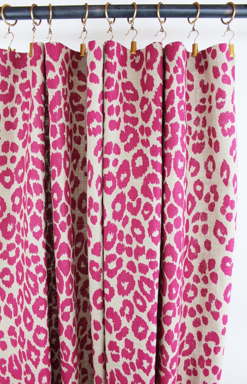 May include: Pink and beige leopard print curtains with a black curtain rod and gold hooks.