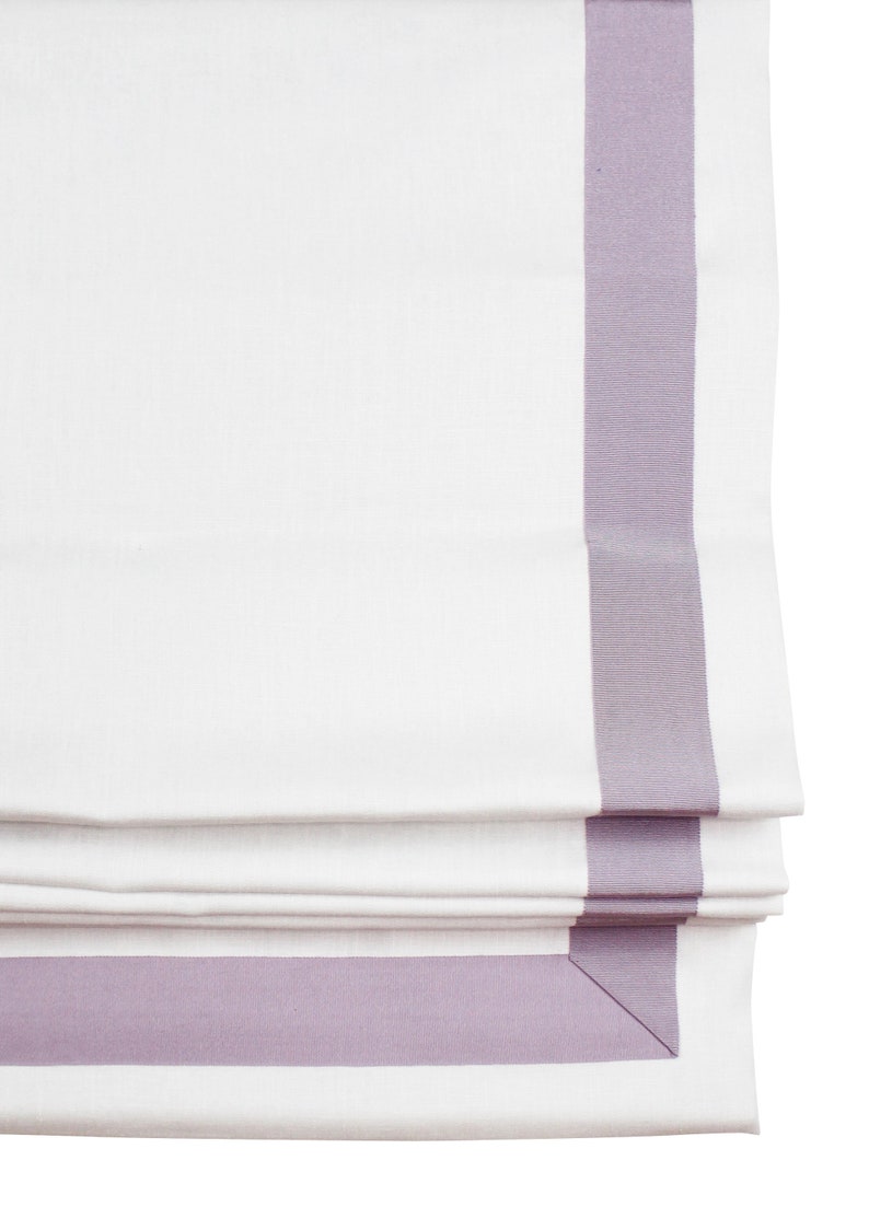 May include: White roman shade with a lavender trim. The shade is folded and the trim is visible on the top and bottom of the shade.