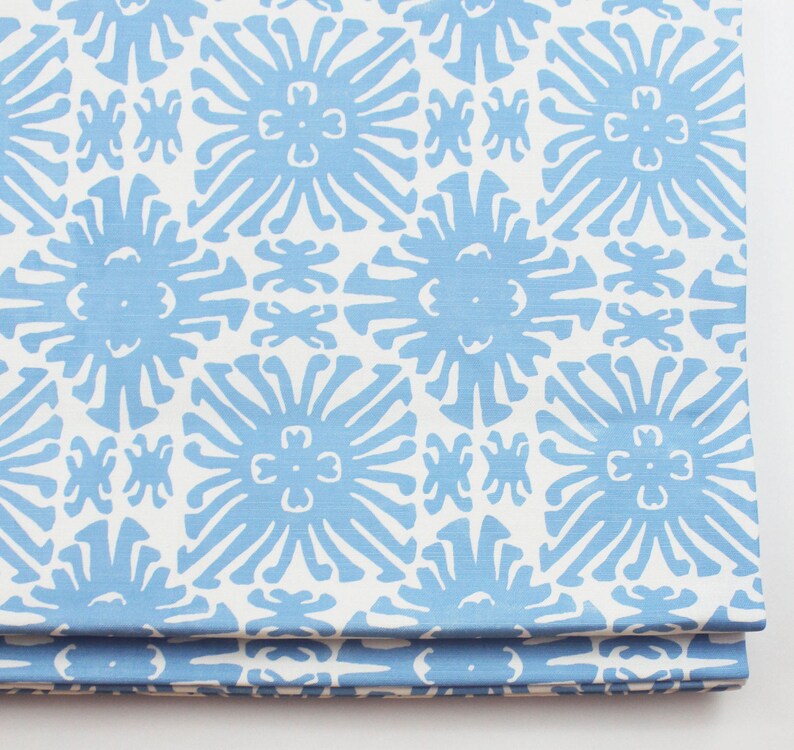 May include: A blue and white fabric with a repeating pattern of stylized flowers. The fabric has a subtle texture and a light blue background.