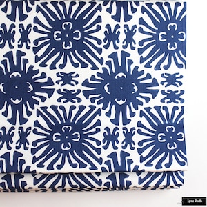 May include: White fabric with a repeating pattern of blue stylized sunbursts. The fabric is folded in thirds.