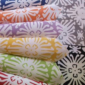 Puede incluir: Una pila de servilletas de tela dobladas en varios colores: azul, naranja, morado, amarillo, verde y rojo. Cada servilleta presenta un estampado floral blanco. El fondo muestra m&aacute;s servilletas en gris y negro.