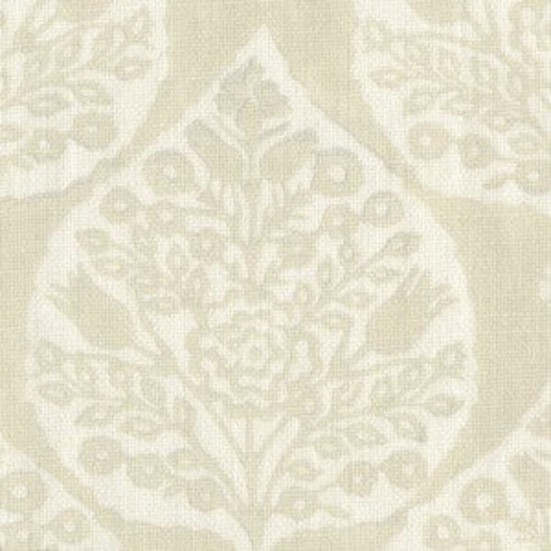Op de afbeelding: Een beige stof met een wit bloemenpatroon. Het patroon heeft een herhalend ontwerp van gestileerde bladeren en bloemen.