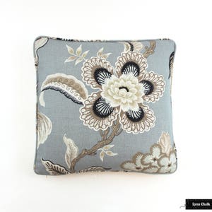May include: A gray pillow with a floral pattern in shades of brown and black. The pillow features a large flower with intricate details and smaller flowers in the corners.