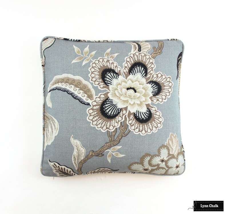May include: A gray pillow with a floral pattern in shades of brown and black. The pillow features a large flower with intricate details and smaller flowers in the corners.