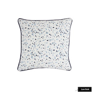May include: A white square cushion with a blue and light blue speckled pattern. The cushion has a dark blue trim around the edges.