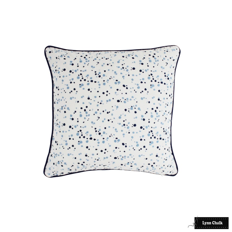May include: A white square cushion with a blue and light blue speckled pattern. The cushion has a dark blue trim around the edges.