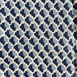 May include: Close-up of a fabric with a repeating geometric pattern. The design features a series of interlocking shapes in shades of navy blue, light blue, and off-white. The pattern creates a textured, visually appealing surface.