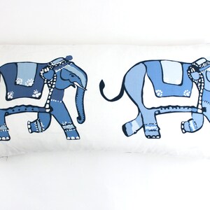 Puede incluir: Una almohada rectangular blanca con dos elefantes estilizados azules impresos en ella. Los elefantes est&aacute;n mirando en direcciones opuestas y tienen mantas de silla con patrones azules y blancos.