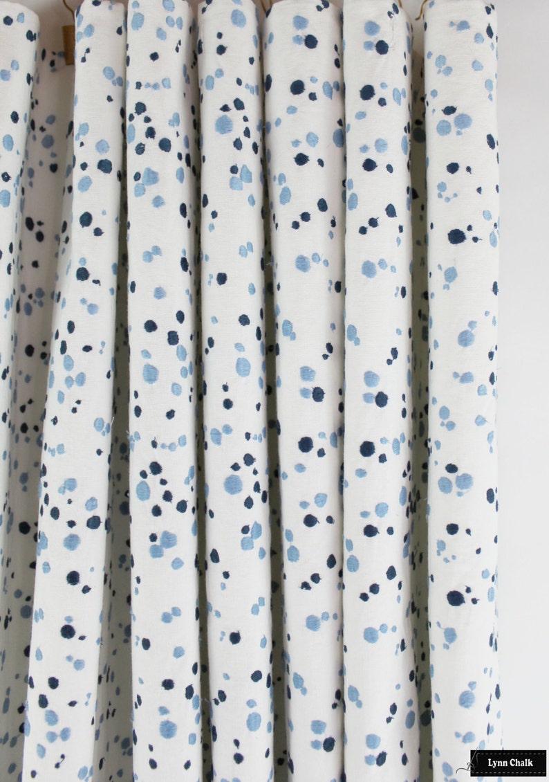 May include: White fabric with a blue and light blue speckled pattern. The fabric is pleated and appears to be a curtain.