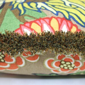 May include: A brown throw pillow with a colorful floral pattern and a brown fringe trim.
