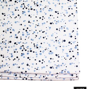 Op de afbeelding: Witte stof met een blauw en zwart gevlekt patroon. De stof is in drie&euml;n gevouwen.