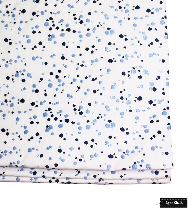 Op de afbeelding: Witte stof met een blauw en zwart gevlekt patroon. De stof is in drie&euml;n gevouwen.