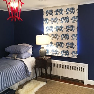 Puede incluir: Una cortina de ventana con estampado azul y blanco con un dise&ntilde;o de elefantes. La cortina est&aacute; colgada en una habitaci&oacute;n con una pared azul, una cama con un edred&oacute;n a rayas azul y blanco, una alfombra blanca y una mesita de noche de madera con una l&aacute;mpara.