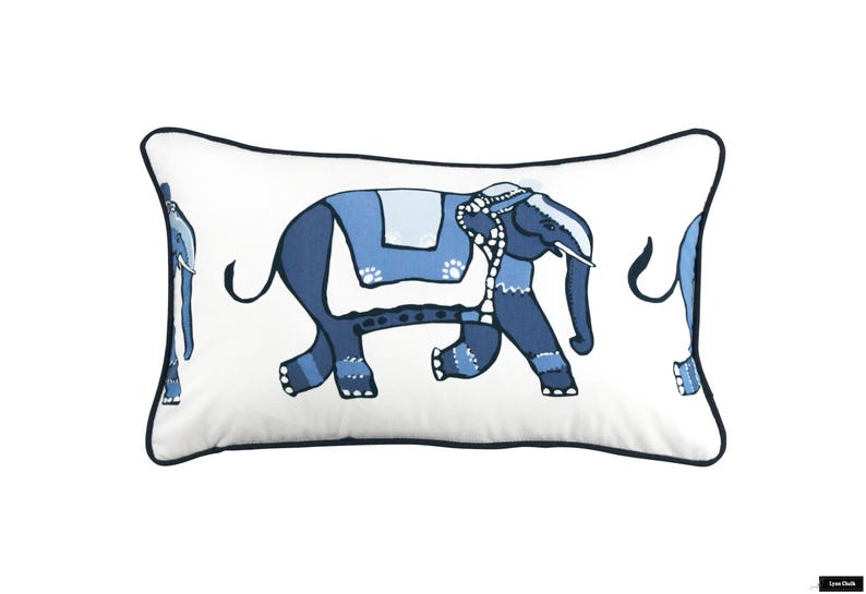 Puede incluir: Una almohada rectangular blanca con un dise&ntilde;o de elefante azul y blanco. El elefante camina hacia la derecha y tiene una silla de montar con estampado azul y blanco.