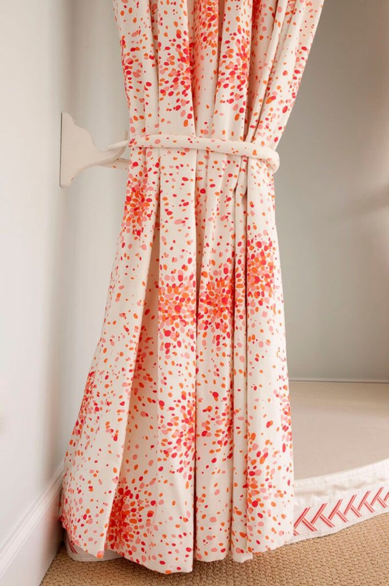 May include: White curtains with a red and orange confetti pattern. The curtains are tied back with a white rope and are hanging from a white hook.