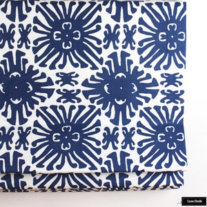 Puede incluir: Primer plano de una tela doblada con un patr&oacute;n repetitivo. El dise&ntilde;o presenta formas florales estilizadas en azul marino sobre un fondo blanco. La tela tiene una apariencia texturizada y un borde color crema.
