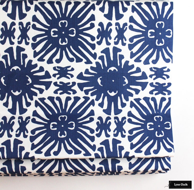 Puede incluir: Primer plano de una tela doblada con un patr&oacute;n repetitivo. El dise&ntilde;o presenta formas florales estilizadas en azul marino sobre un fondo blanco. La tela tiene una apariencia texturizada y un borde color crema.