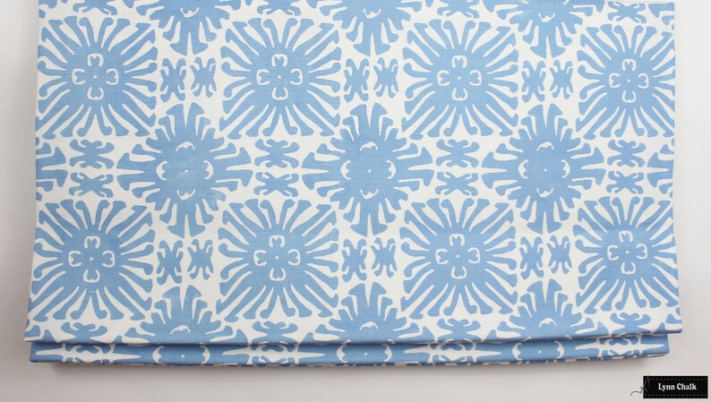 Puede incluir: Tela doblada con un patr&oacute;n repetitivo de dise&ntilde;os florales azul claro sobre un fondo blanco. El patr&oacute;n floral es un dise&ntilde;o estilizado y sim&eacute;trico. La tela parece ser un textil decorativo, posiblemente para la decoraci&oacute;n del hogar.