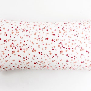 Op de afbeelding: Een wit rechthoekig kussen met een roze en rood splatterpatroon.